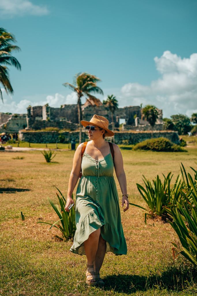 Woman walking in a green dress with Mayan ruins of Tulum in the background