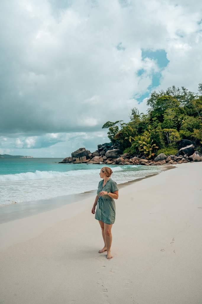 Woman standing on a white sand beach looking behind her to the water and shoreline