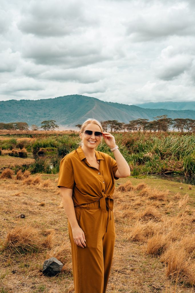 Woman wearing a full neutral outfit looking at camera with Ngorongoro Crater in the background