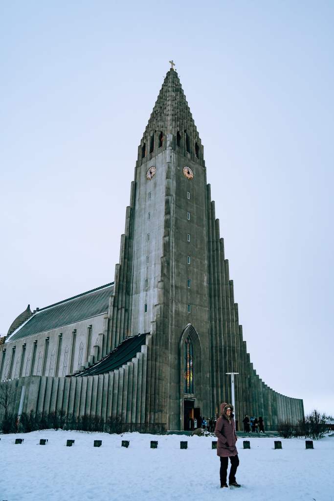 Woman standing in front of the Hallgrimskirkja Churck, which looks like a spaceship, in Iceland