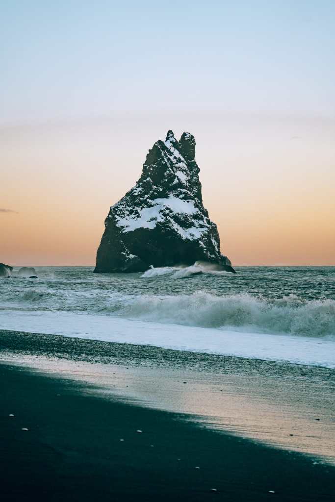 Seastack on Reynisfjara Black Sand Beach in Iceland with a sunset sky behind it