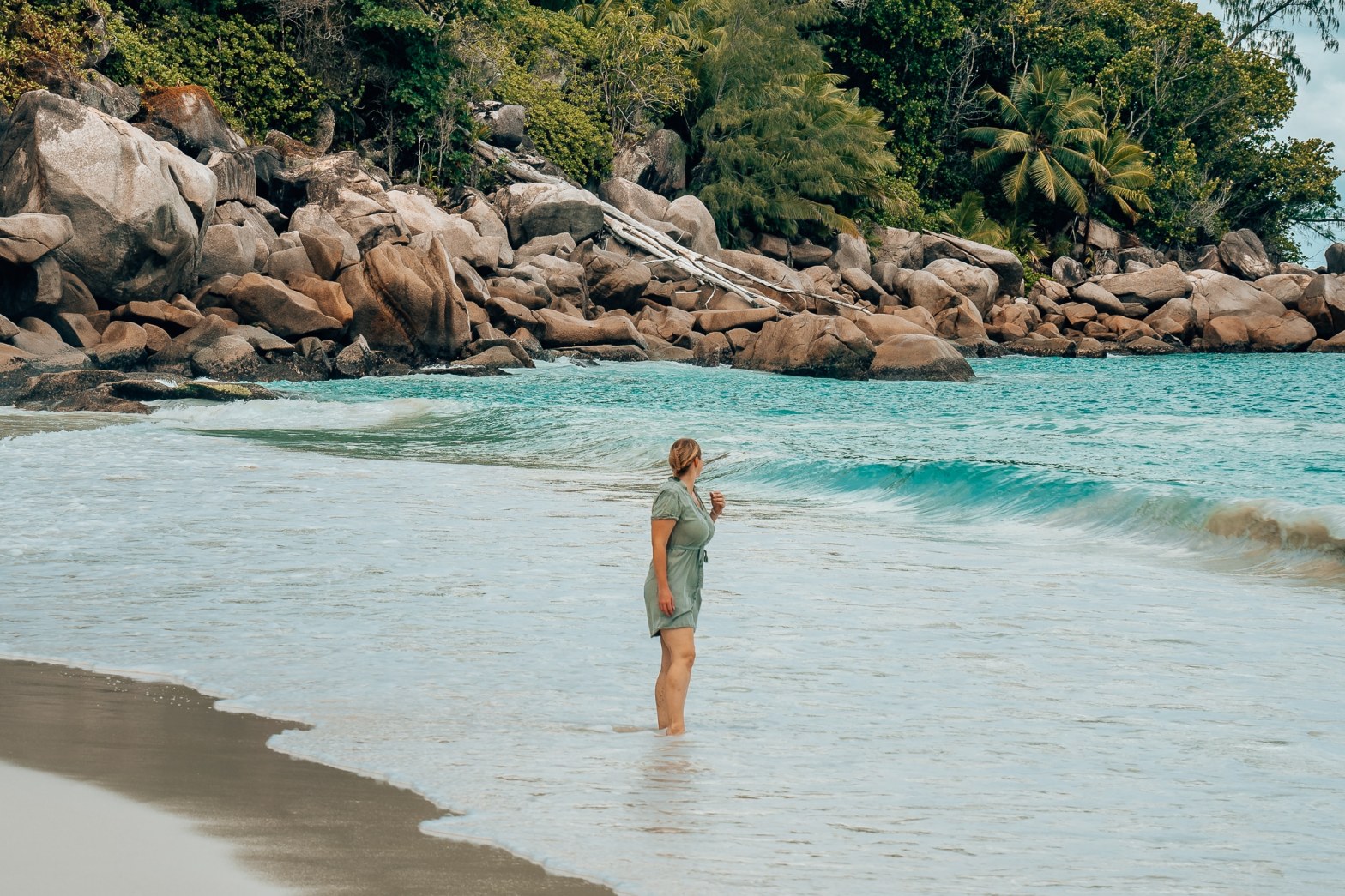 Woman in a green dress standing about ankle deep at a beach on the Seychelles looking off to the water