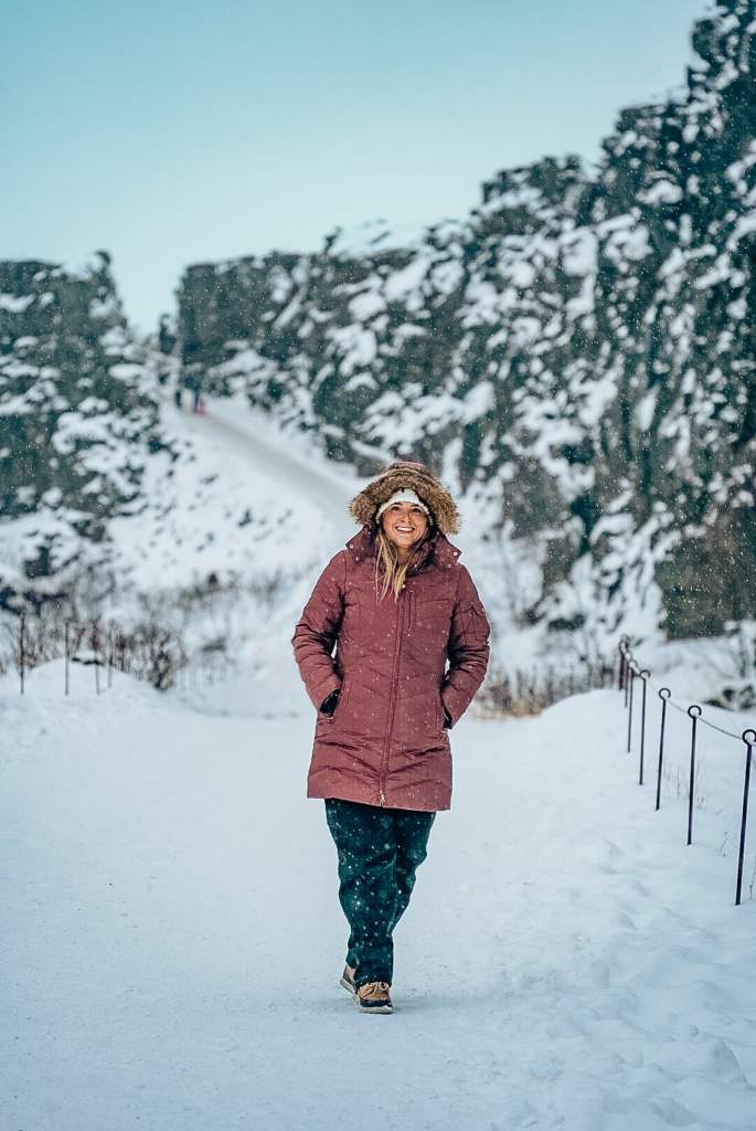 Woman standing in the snow while it's snowing with the continental divide in Thingvellir National Park behind