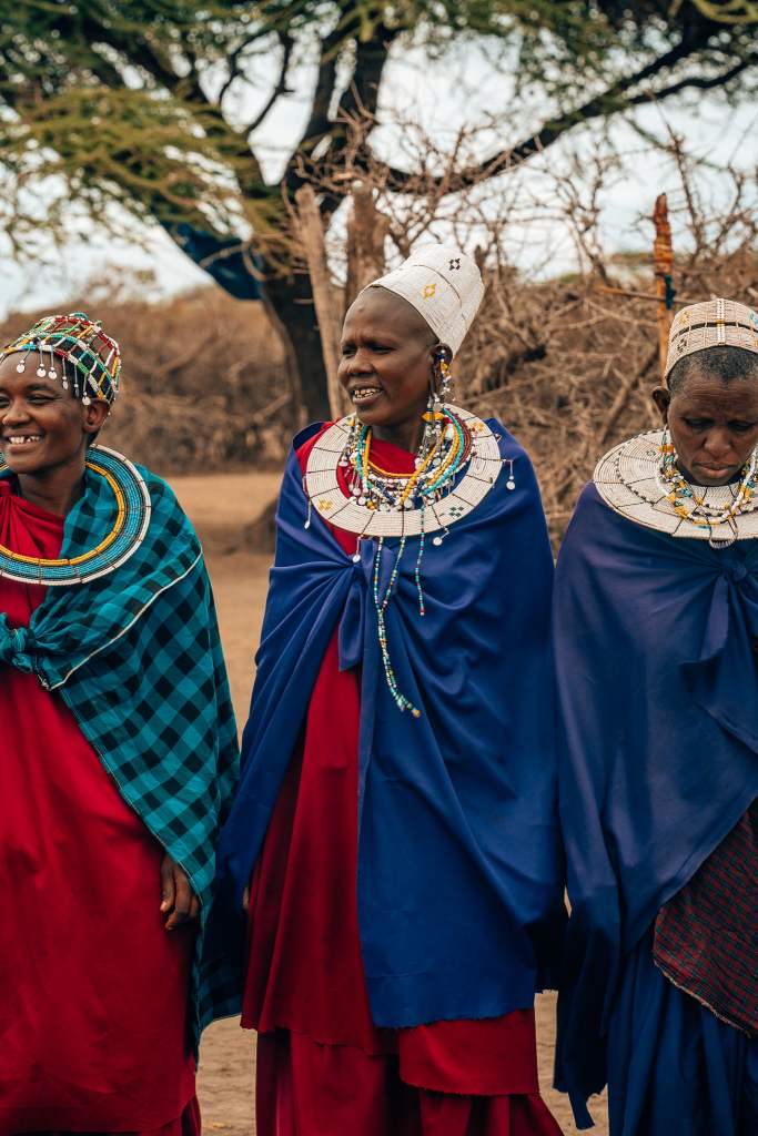 3 women of the Maasai tribe in Tanzania standing in their village adorned in their gear