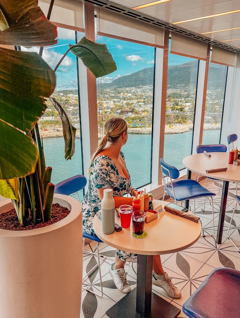 Woman sitting at a table with drinks and food on it looking out through the windows of the cruise ship to Puerto Plata, Dominican Republic