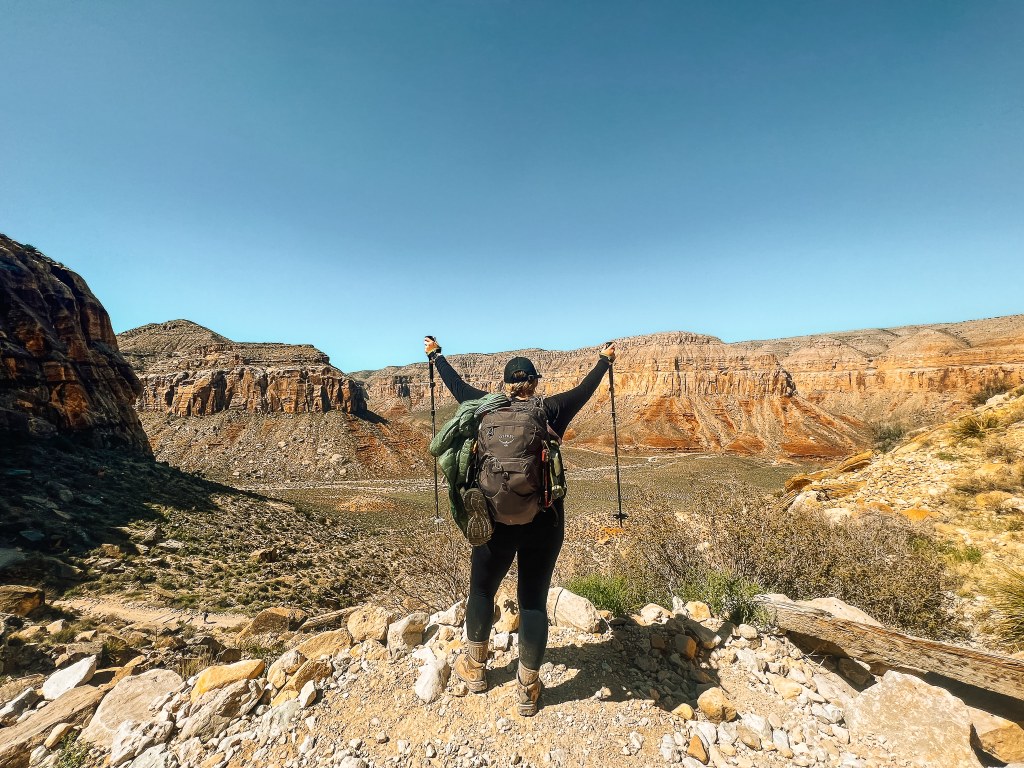 Woman with her hiking backpack and gear holding up her hiking poles looking out to the canyon