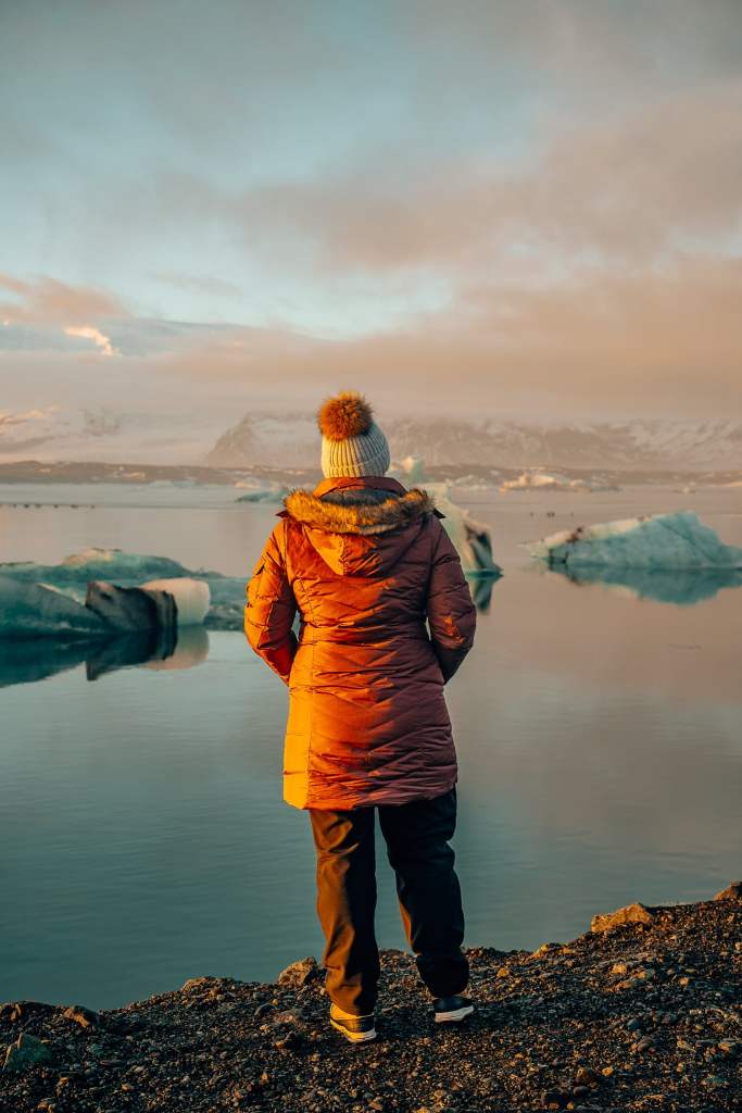 Woman standing at sunset looking out to glacier lagoon