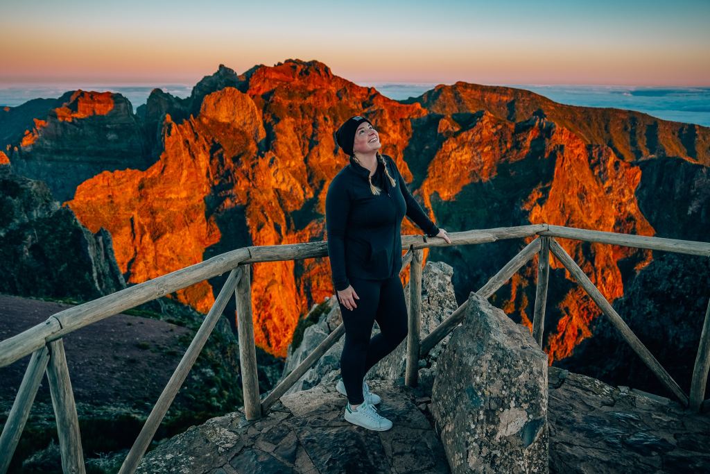 Smiling woman standing in front of sunrise-stained mountains in Madeira