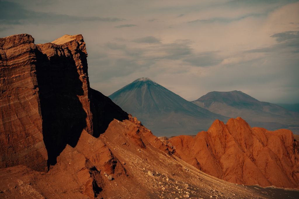 View of the volcano from Valle de la Luna in the Atacama Desert with large red rocks jutting out in front