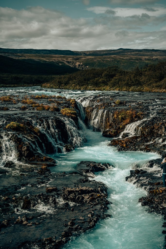 View of Bruarfoss waterfall in Iceland where light blue water flows over black lava rock