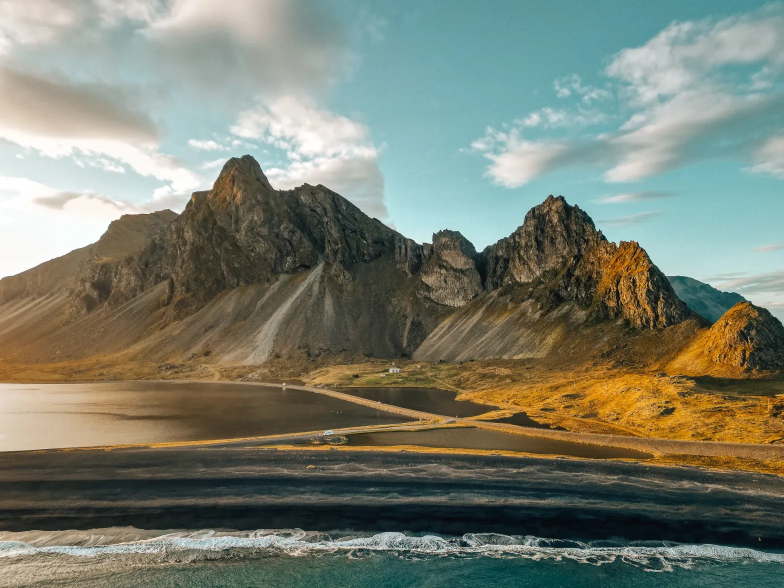 Drone view of Eystrahorn mountain in Iceland from above the water, with a black sand beach and the mountain visible behind