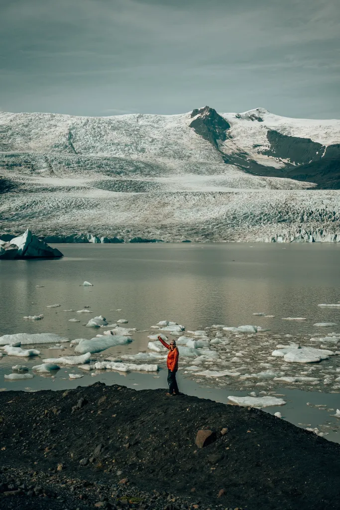 Woman standing on black volcanic rock with Iceland's Fjallsjokull glacier in the background
