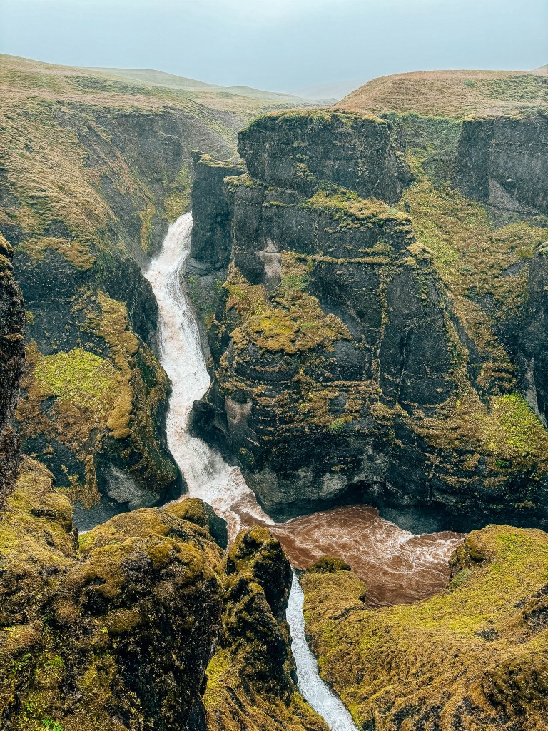 View of Fjaðrárgljúfur Canyon looking toward the waterfall where it cascades down the lava rock