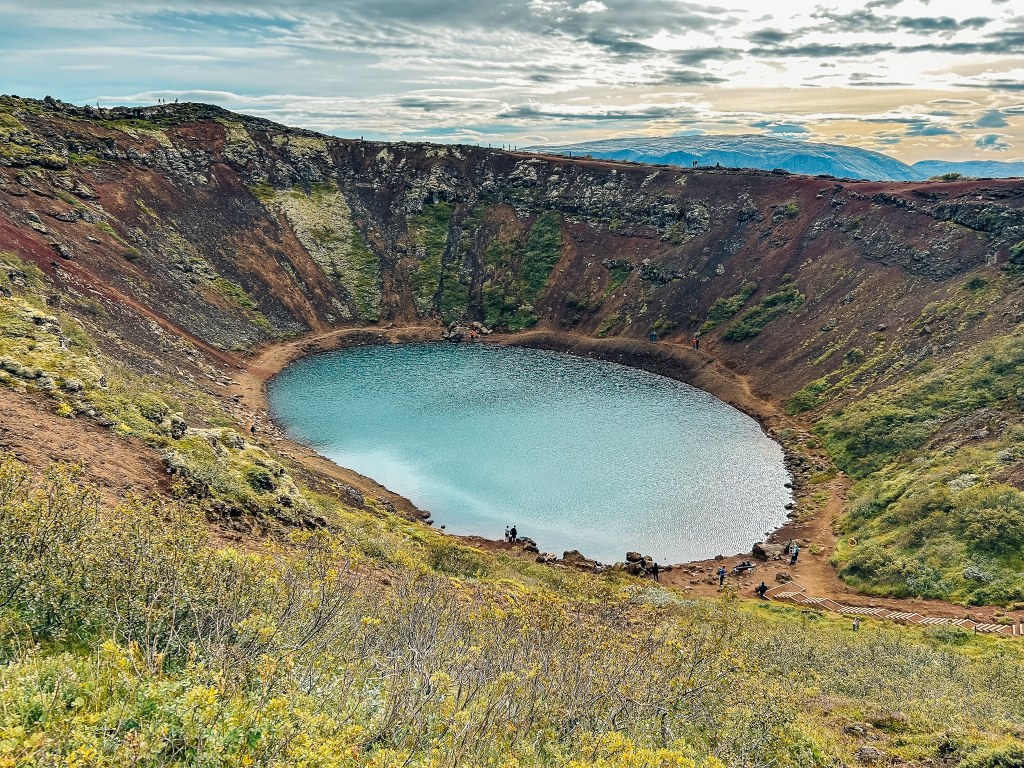 View of Kerid Crater at the top, with green mossy walls and bright blue water of a lake at the bottom
