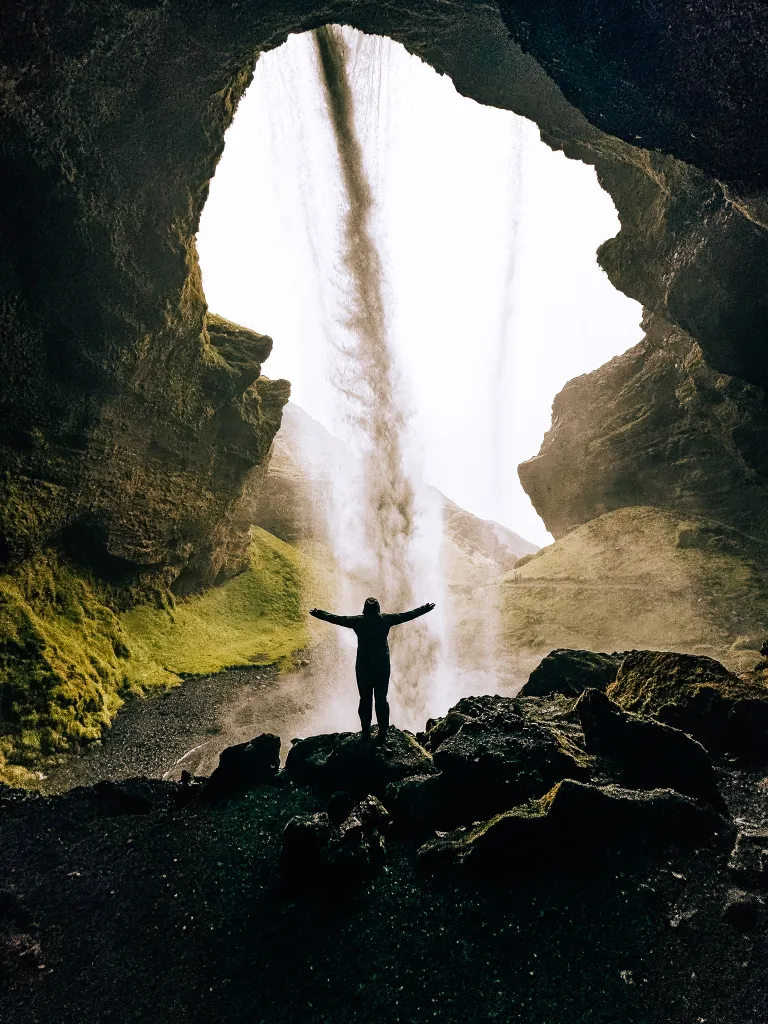 Woman standing behind Kvernufoss waterfall in Iceland looking out to the river