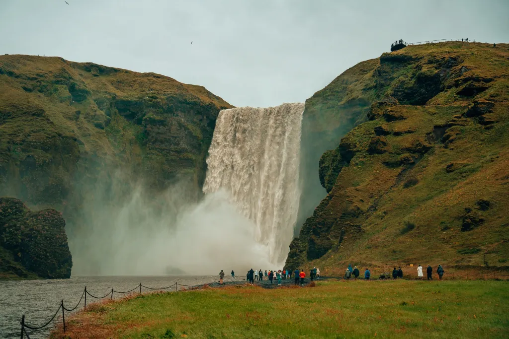 View of Skogafoss waterfall in Iceland seeing the water fall from the green cliff with people standing in front of the water