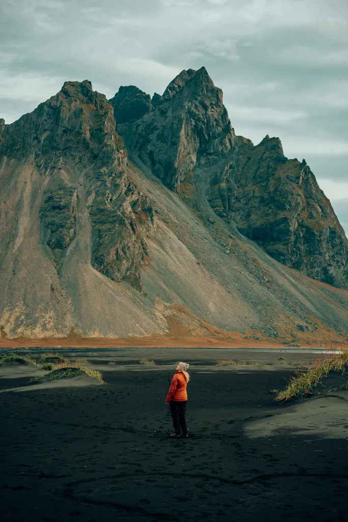 Woman standing on a black sand beach with Iceland's famous Vestrahorn mountain in the background