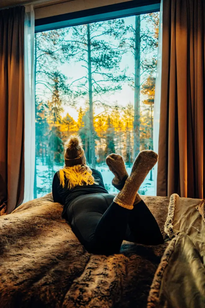 Woman lying on a bed looking out the window of her lodge in Lapland, Finland