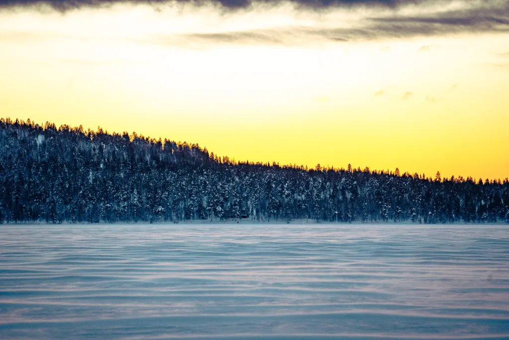 Snow snakes blowing over a frozen Lapland lake with the sunset in the background