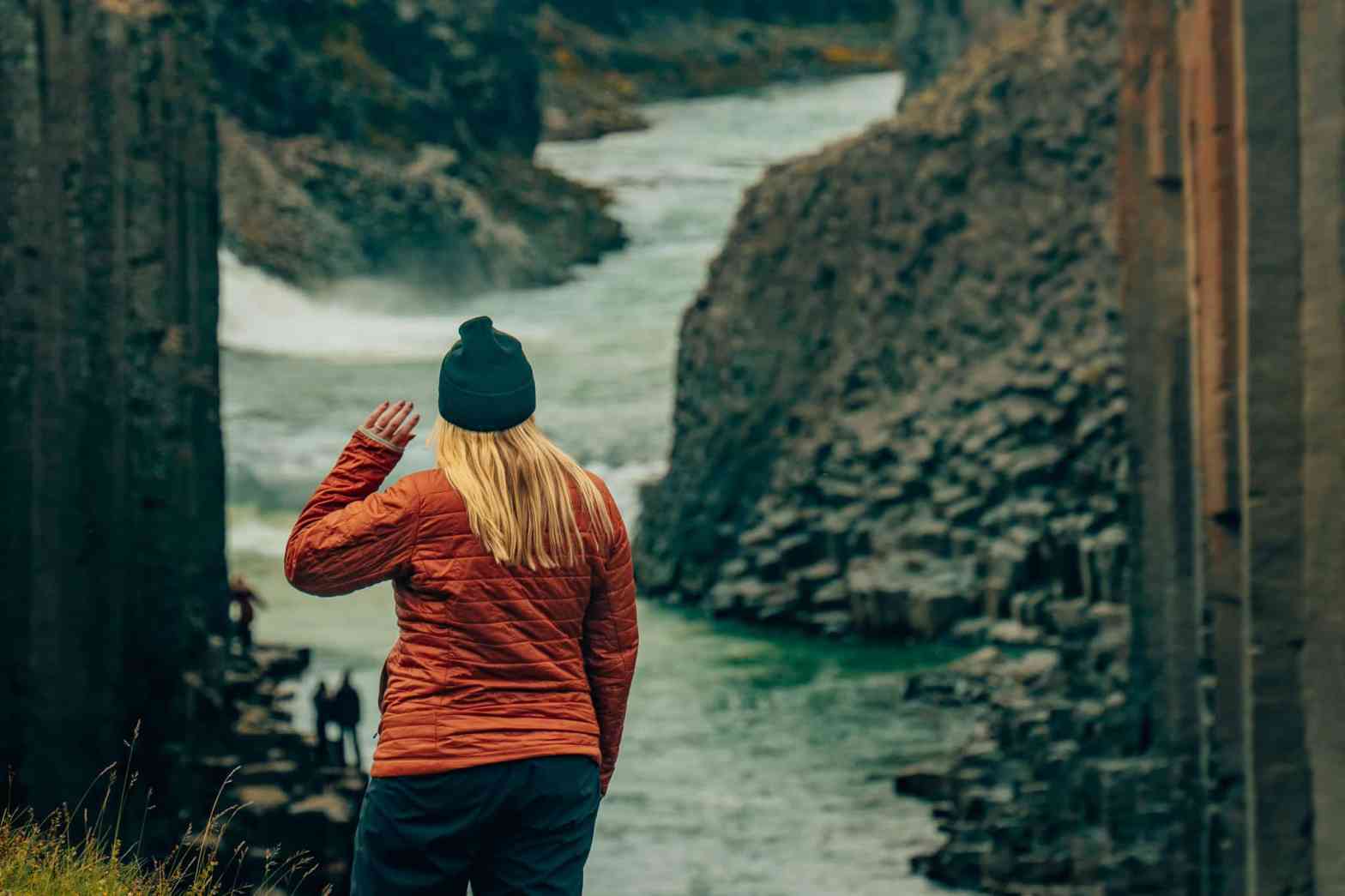 Woman in a puffer jacket looking away from the camera, looking at Studlagil canyon in Iceland