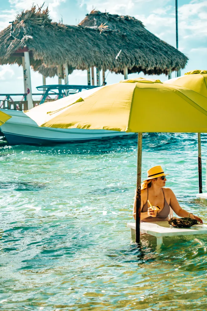Woman sitting in the ocean water unter a green unbrella with a pier in the background
